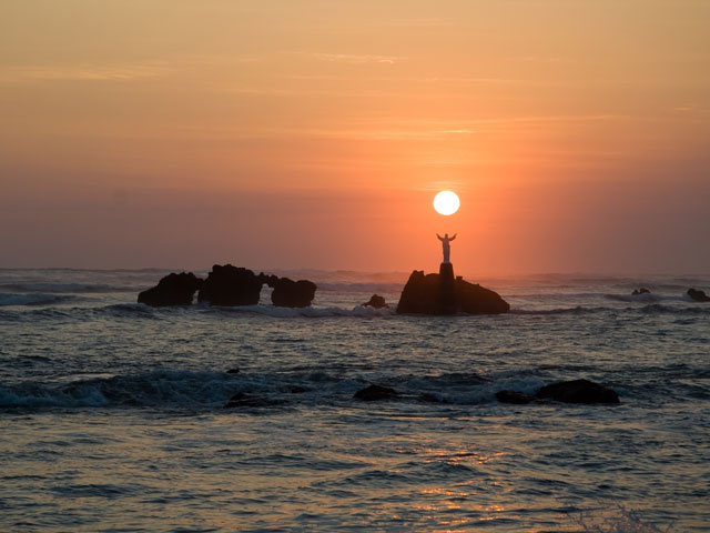 The sun sets over a statue of Jesus out in the ocean in El Salvador