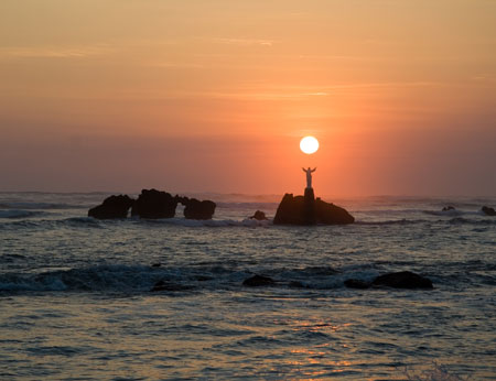 The sun sets over a statue of Jesus out in the ocean in El Salvador