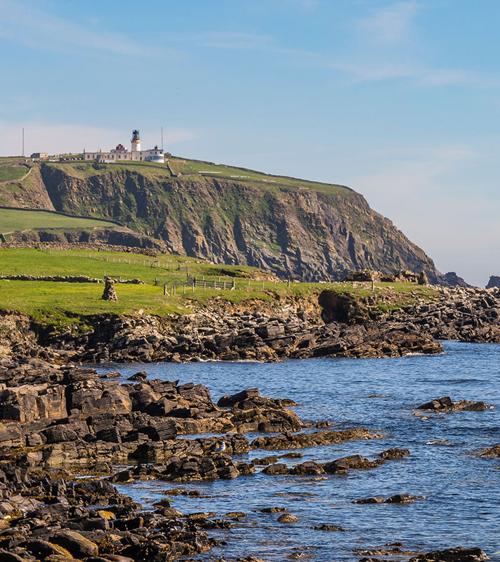 View along the rocky beach with the Sumburgh Head lighthouse behind View along the rocky beach with the Sumburgh Head lighthouse behind