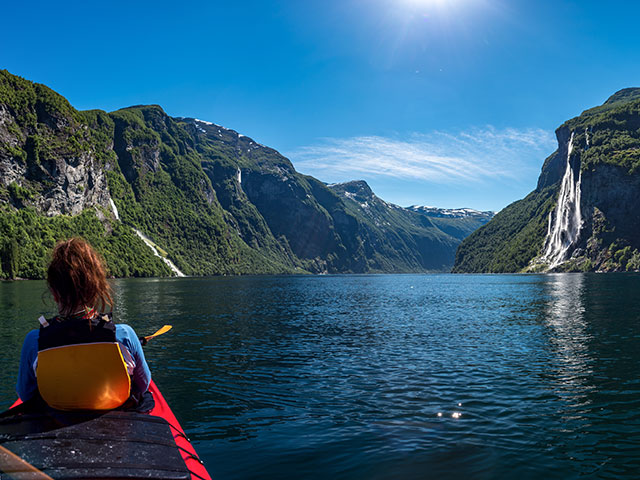Girl floating on a kayak over the Geiranger fjord overlooking the waterfall of seven sisters in Norway