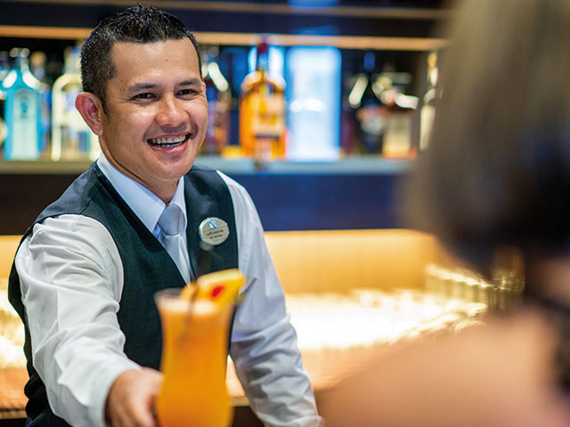 Waiter smiling and serving a cocktail to guest in The Piano Bar