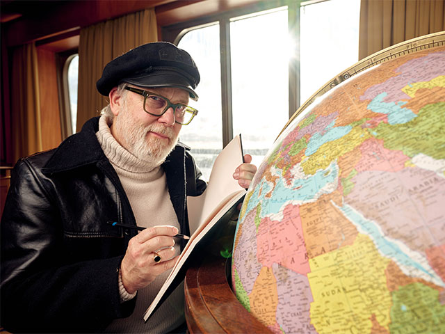 Jim Moir (AKA Vic Reeves) with globe in the library on board Bolette