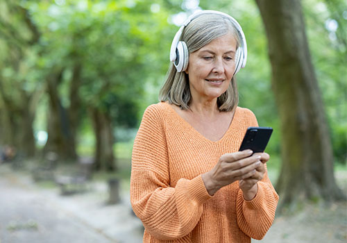 Mature woman wearing headphones using smartphone in park. 