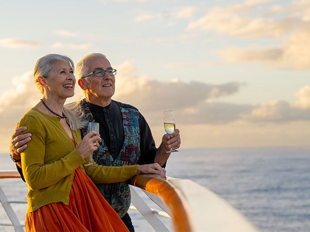 Guests on deck with drinks, looking out to sea