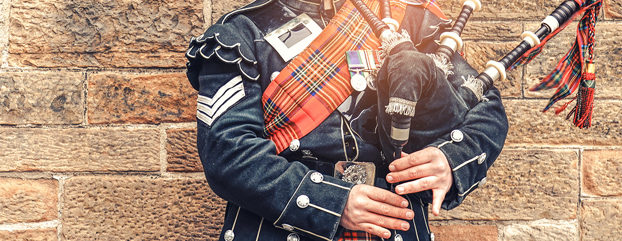 Traditional Scottish bagpiper, dressed in red and black tartan 