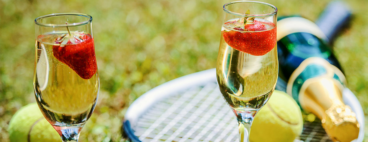 Tennis game. Strawberries, champagne and tennis balls with rackets on the green grass. 