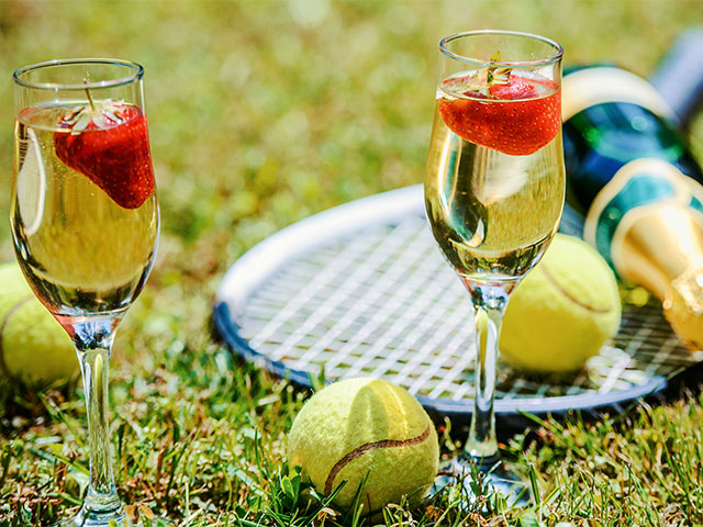 Tennis game. Strawberries, champagne and tennis balls with rackets on the green grass. 