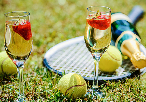 Tennis game. Strawberries, champagne and tennis balls with rackets on the green grass. 