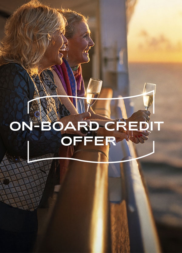 On-board credit offer. Two smiling guests holding glasses of sparkling wine lean on a ship's railing at sunset, looking out to sea.