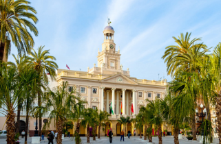 Cádiz City Hall, a neoclassical building with a clock tower, framed by palm trees on a sunny plaza.